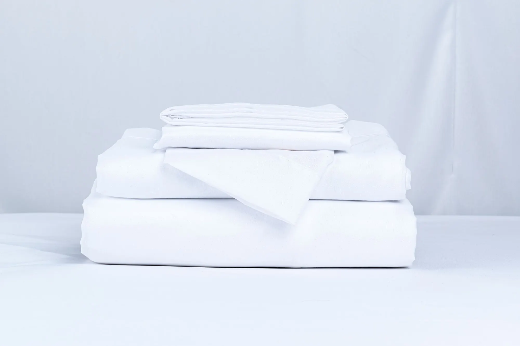 A neat stack of folded white bed sheets and pillowcases.