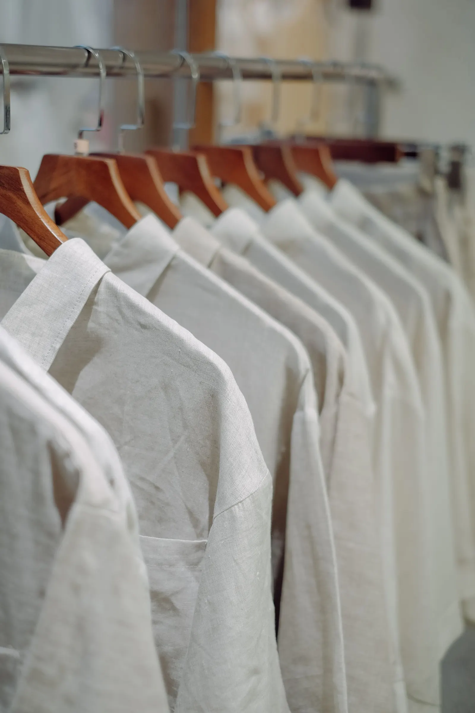 A row of pressed linen shirts on wooden hangers along a rail.